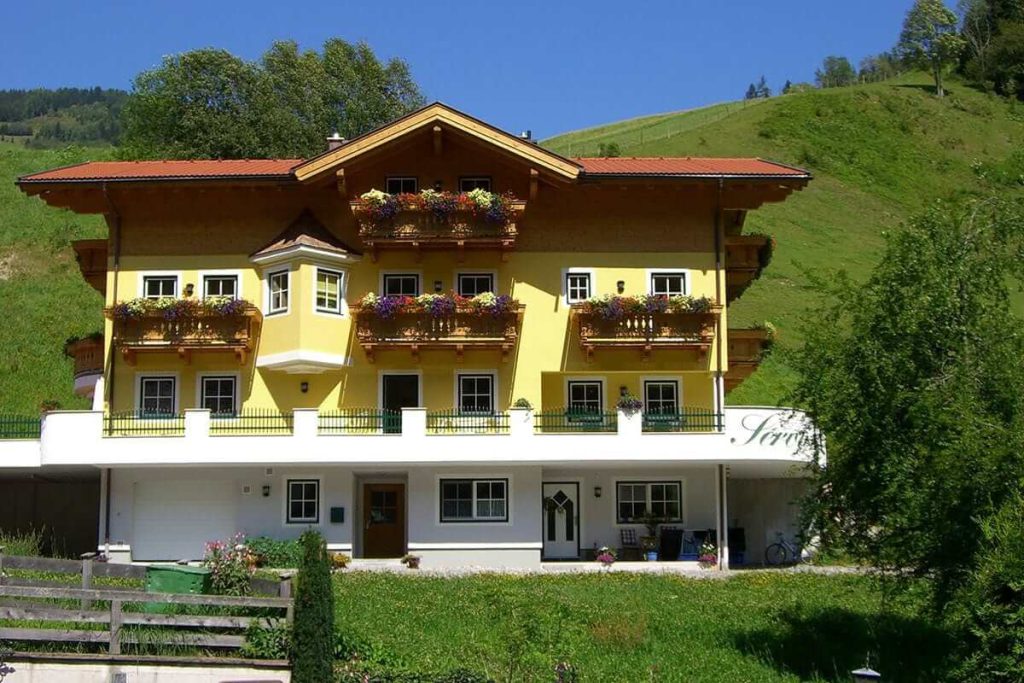 Helles Landhaus Servus in Viehhofen, umgeben von grünen Hügeln und Blumenbalkonen.
